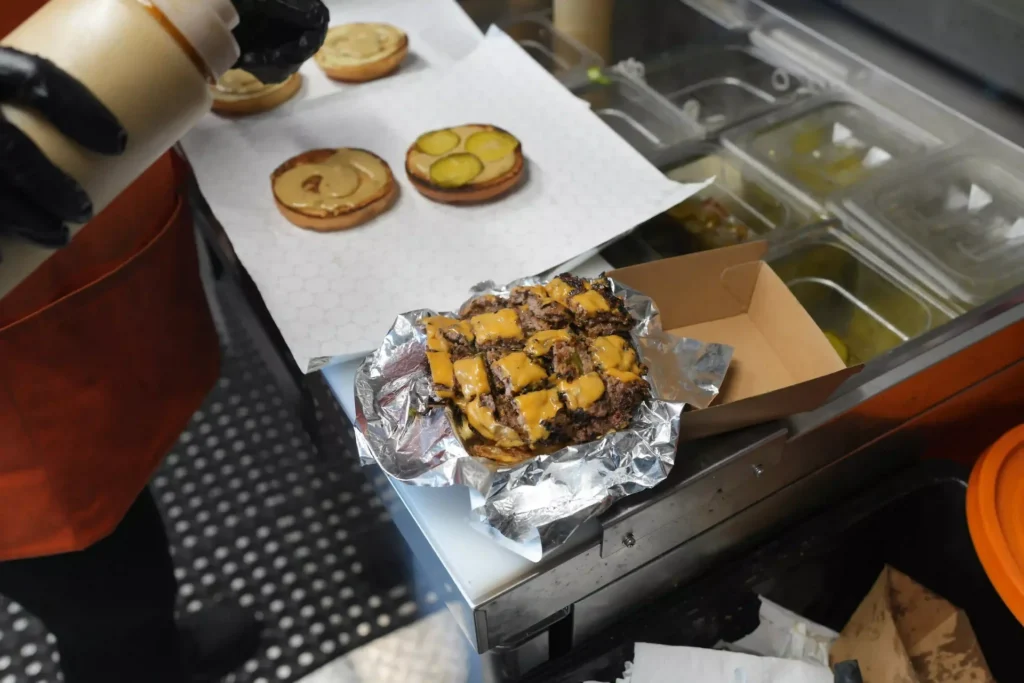 Burger buns with pickles on parchment beside a foil-wrapped burger inside the trailer